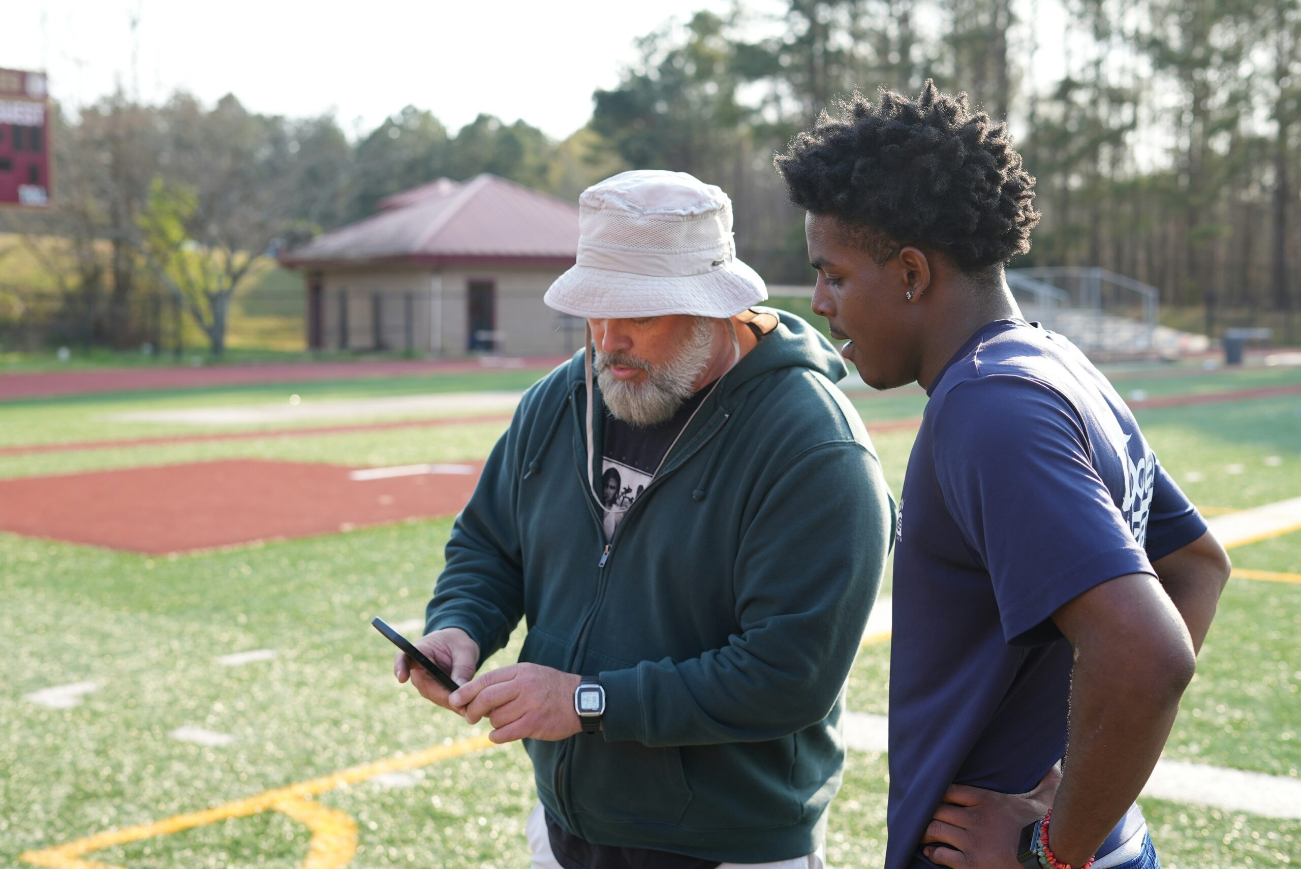 Coach in bucket hat showing athlete a video on phone.