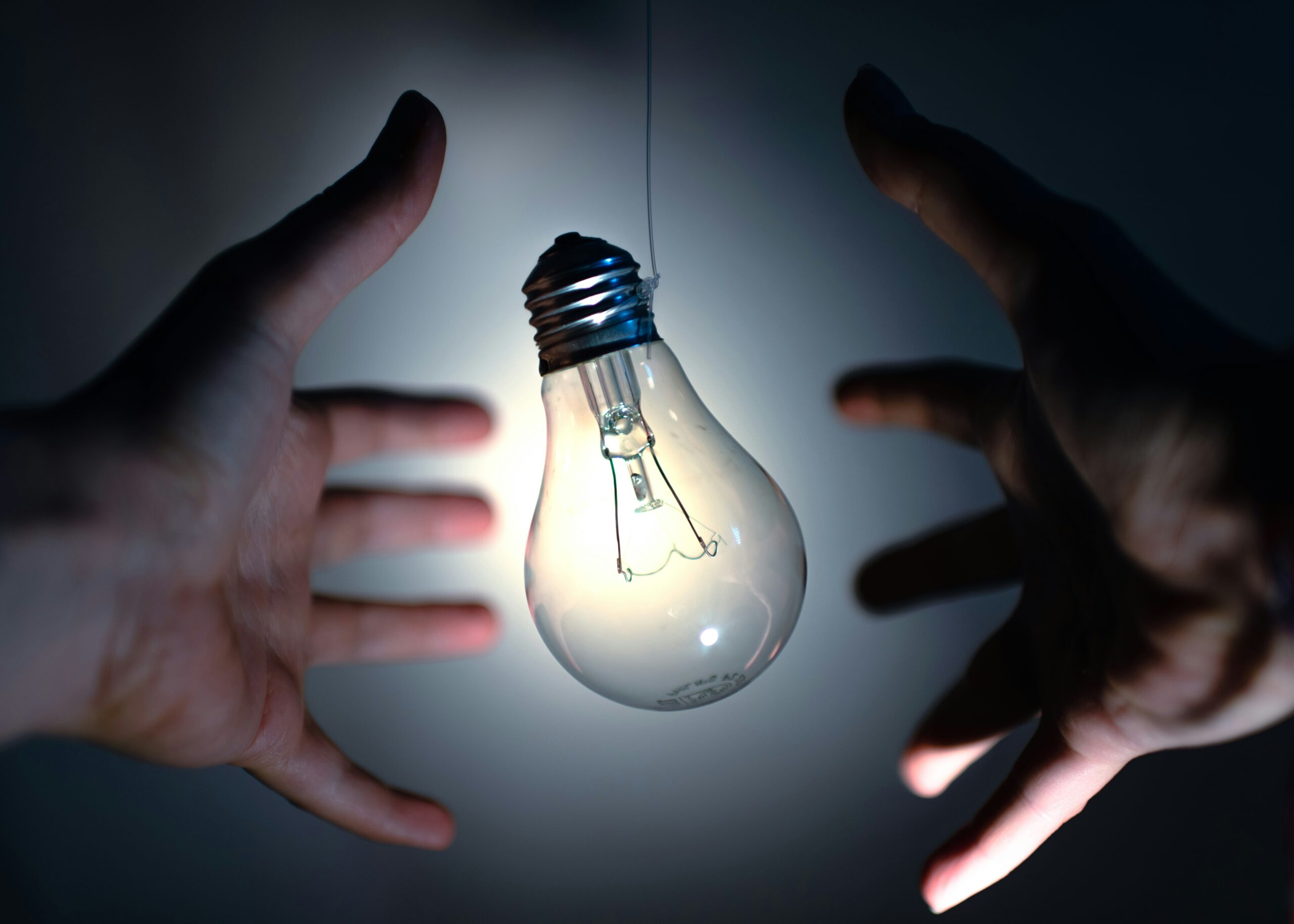 Two hands reaching for lightbulb like a group reaches for ideas and learning.